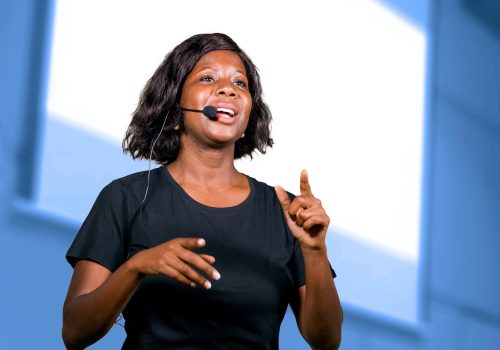 young attractive and successful black afro American entrepreneur woman with headset speaking in auditorium at corporate training event or seminar giving motivation and success coaching conference